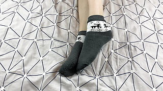 Girl with long legs caresses her feet in gray New Year socks with deer